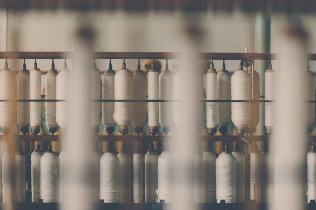 Rows of white cotton thread spools arranged on textile-manufacturing equipment.
